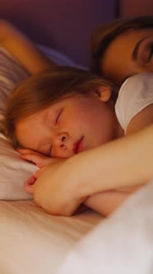 Sleepy Mother Embraces Daughter Lying Together in Bed