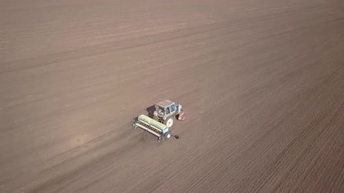 Top Down Aerial View of Green Tractor Cultivating Ground and Seeding a Dry Field