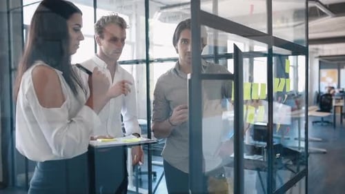 Young business people in formal clothes planning work in the office with paper stickers on the glass