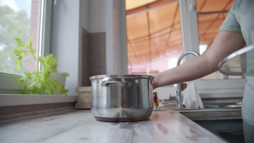 Hand Placing Metal Pot on Kitchen Surface