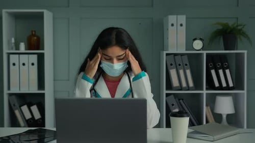 Exhausted Woman Doctor Rubbing Temples at Her Desk