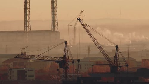 Towering Cranes and Smokestacks Under Golden Sky