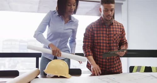 Diverse male and female architects with tablet discussing blueprints standing in office, slow motion
