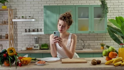 Young Woman at the Table in the Kitchen Preparing Spring Rolls for Healthy Lunch Reading Recipe on