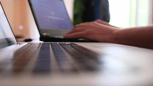 Des mains masculines tapent le code du programme sur différents ordinateurs portables en gros plan, vue latérale inférieure.
