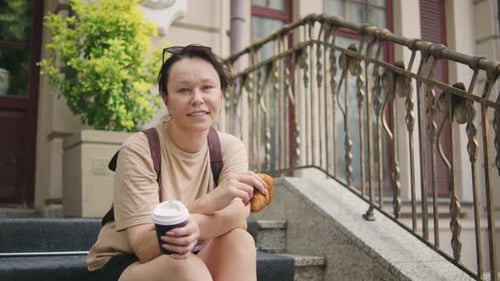 Woman with Coffee and Croissant on City Steps