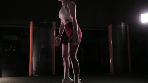Athletic Woman Doing Jump Squats in Dark Gym