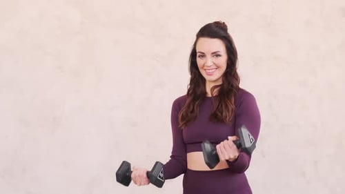 The woman shakes her arms with dumbbells and smiles. Strong woman in the gym. Serious athlete workou