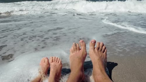 Feet of a father and daughter lying on a sandy beach during a vacation at sea.
