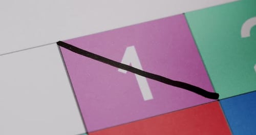 Nahaufnahme der Markierung des ersten Tages auf einem bunten Kalender mit schwarzem Stift