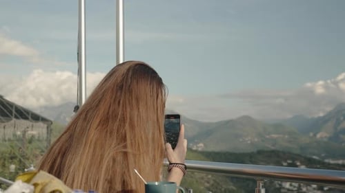A Woman with Long Hair Captures the Mountains on her Smartphone while Standing on a High Peak.