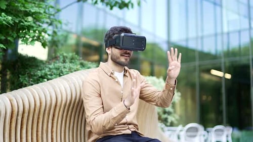 Businessman works using VR glasses in virtual reality simulator sitting on bench on street near