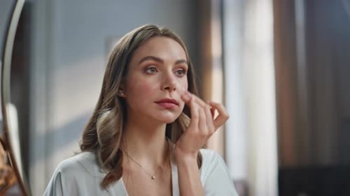 Woman Applying Moisturizer to Face in Mirror