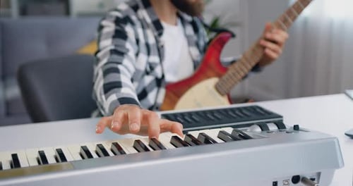 Close up of male hands playing on syntezator playing and guitar. Bearded musician man in headphone r