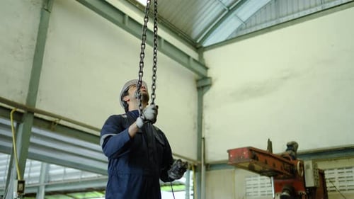O engenheiro de fábrica masculino opera um guincho de corrente elétrico pesado com controle remoto, garantindo