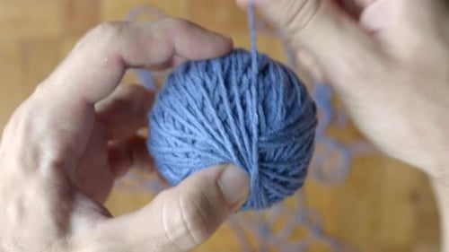 Hand finishing winding ball of blue wool. Static blur background. Top view