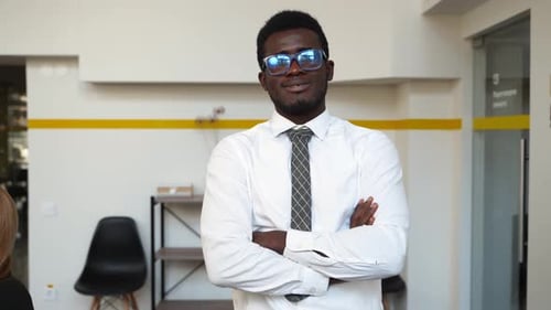 Lächelnder afroamerikanischer Geschäftsmann in formeller Kleidung blickt in die Kamera und steht in Büroarmen