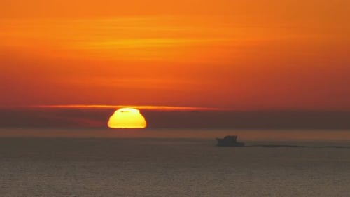 Dramatic slow motion sunrise over ocean. Small motorboat silhouette, orange sun on horizon.