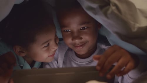 African American Siblings Using Digital Tablet under Blanket