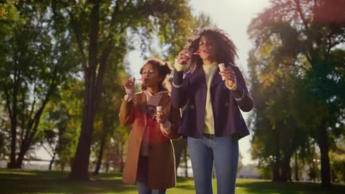 Happy african american family enjoying sweet childhood moments blowing bubbles in park