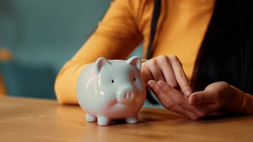 Frau mit langen dunklen Haaren spart Geld in einem Sparschwein in einem gemütlichen Innenraum