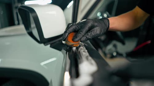 Close-up of a car wash worker using a plastic washing brush while cleaning the door card of a car