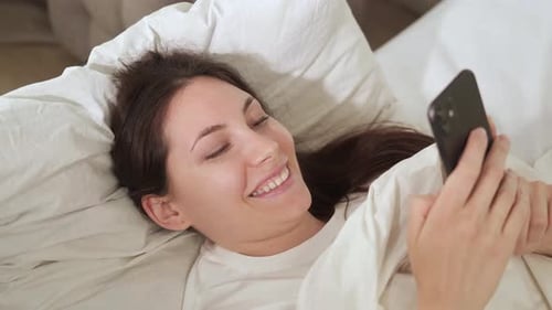 Smiling Woman Using Smartphone in Bed