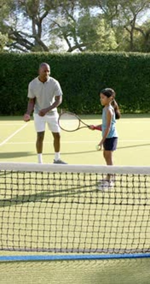 Vertical video: Playing tennis, man coaching young girl on court, focusing on technique