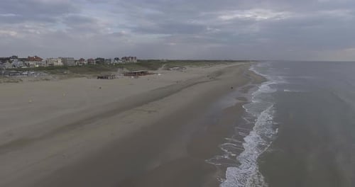 A drone shot by the sea, panning right, waves rolling in and people walking on the beach