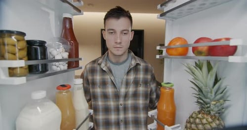 A Young Man Takes a Container with Breakfast From the Refrigerator View From Inside the Refrigerator