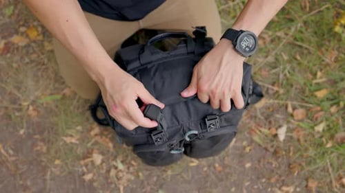 Les
mains roulent le haut d'un sac pour le fermer. Un randonneur masculin attache des sangles avec des boucles sur le dessus de son sac à dos de
randonnée