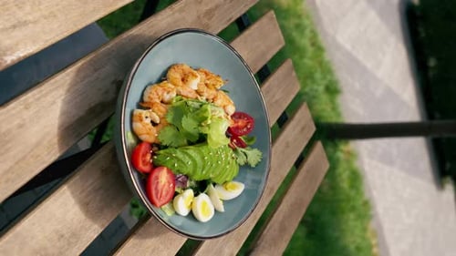 Close Up in a Restaurant on the Street on Plank Table a Blue Plate with a Warm Salad with Avocado