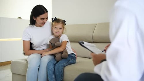 Mother with her daughter that with teddy bear have a consultation in the clinic with male doctor