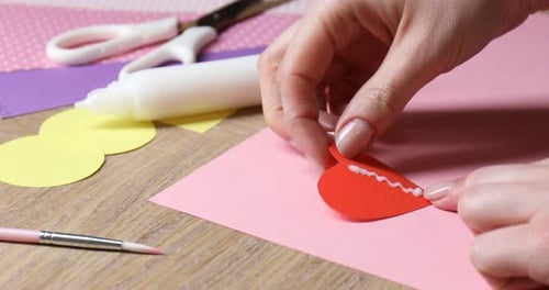 Hands Gluing Paper Heart on Pink Cardstock