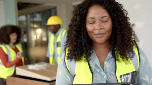 Smiling casual biracial female architect with tablet in office, slow motion, copy space