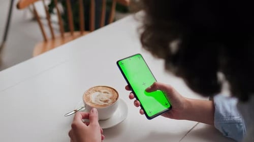 Cafe girl drinks cappuccino holds a cup of coffee and looks at the screen of the smartphone on which