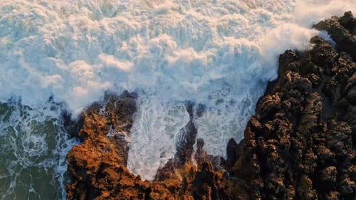 Vue aérienne : vagues océaniques orageuses brisant des roches volcaniques, paysage fluvial