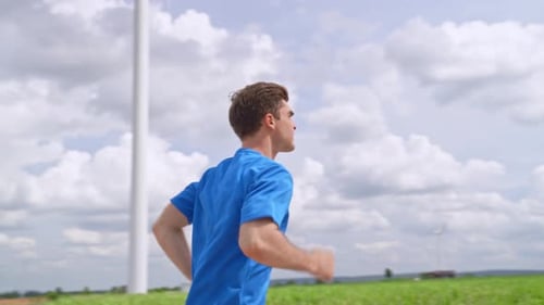 Caucasian active sportsman running exercise at the wind turbine field.