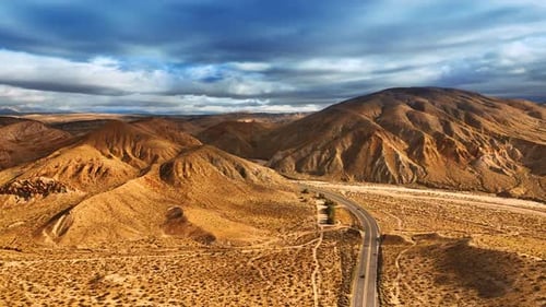 Dry desert with no greenery. Drone rising above the highway opening the view on bare mountains.
