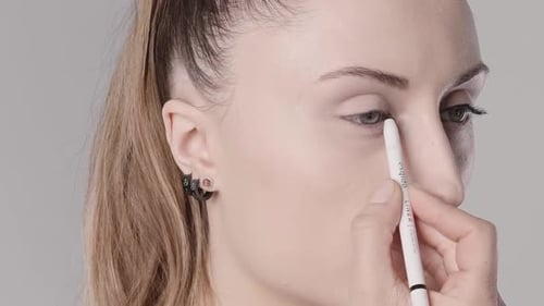 A young woman draws eyeliner on her eyes