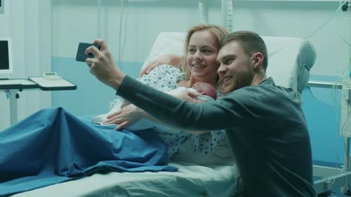 Father Takes Selfie of Him with His Wife Holding Newborn Baby while Lying on the Hospital Bed. Happ