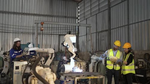 Blue collar workers are working at machine shop with welding robot arm.