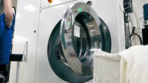 Woman Opening Industrial Washing Machine in Laundry