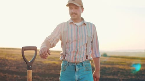 Portrait of Positive Adult Male Farmer Wearing Hat Staying at the Field and Smiling to the Camera