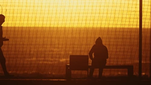 Menschen bei Sonnenuntergang Ein ruhiger Moment, eingefangen durch eine Person, die auf einer Bank vor einem Zaun sitzt