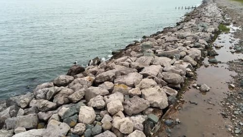 Aerial view above splashing ocean tide breaking on rocky coastal shoreline slow push in