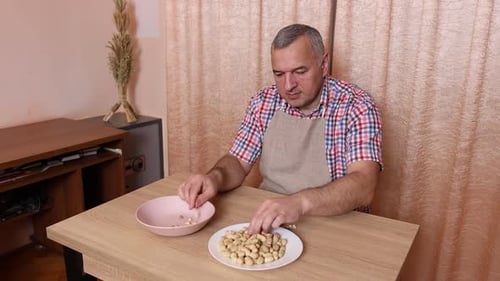 Man Shelling Peanuts at Table in Bright Room