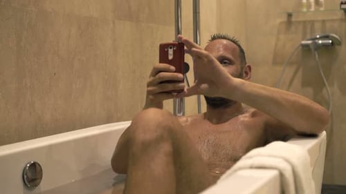 Man in bathtub taking selfie with phone