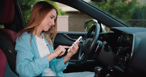 Young woman is sitting in the driver's seat using a touch display screen multimedia device in car
