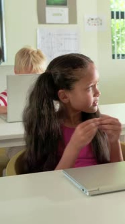 Vertical video: Reacting to cue, girl in pink top fixing hair, clapping in class with shut laptop